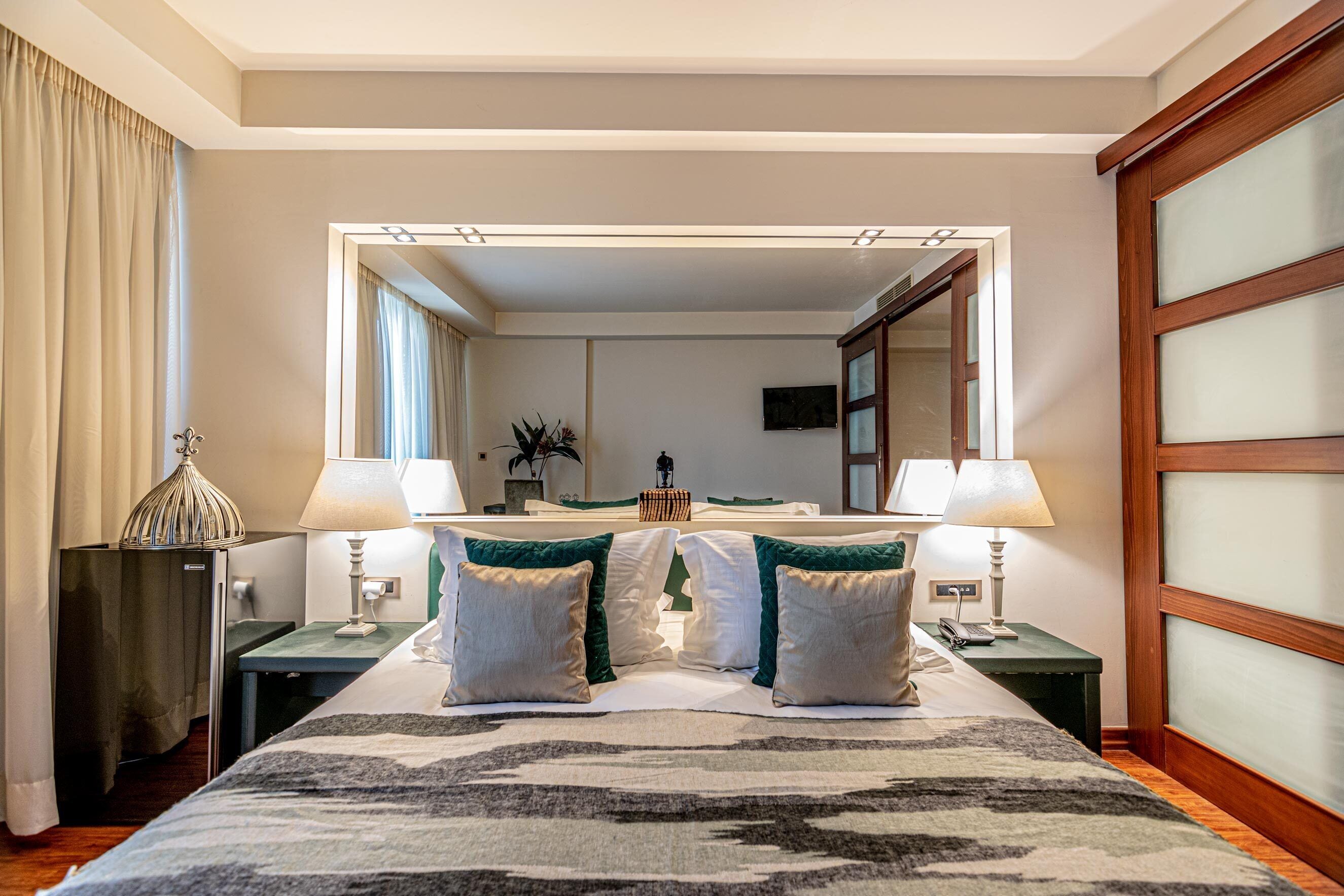 A hotel room with a large bed, two bedside tables, a mirror, and a television.