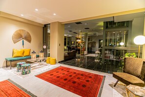 A modern lobby with a sofa, armchairs, a fan, and a red rug.