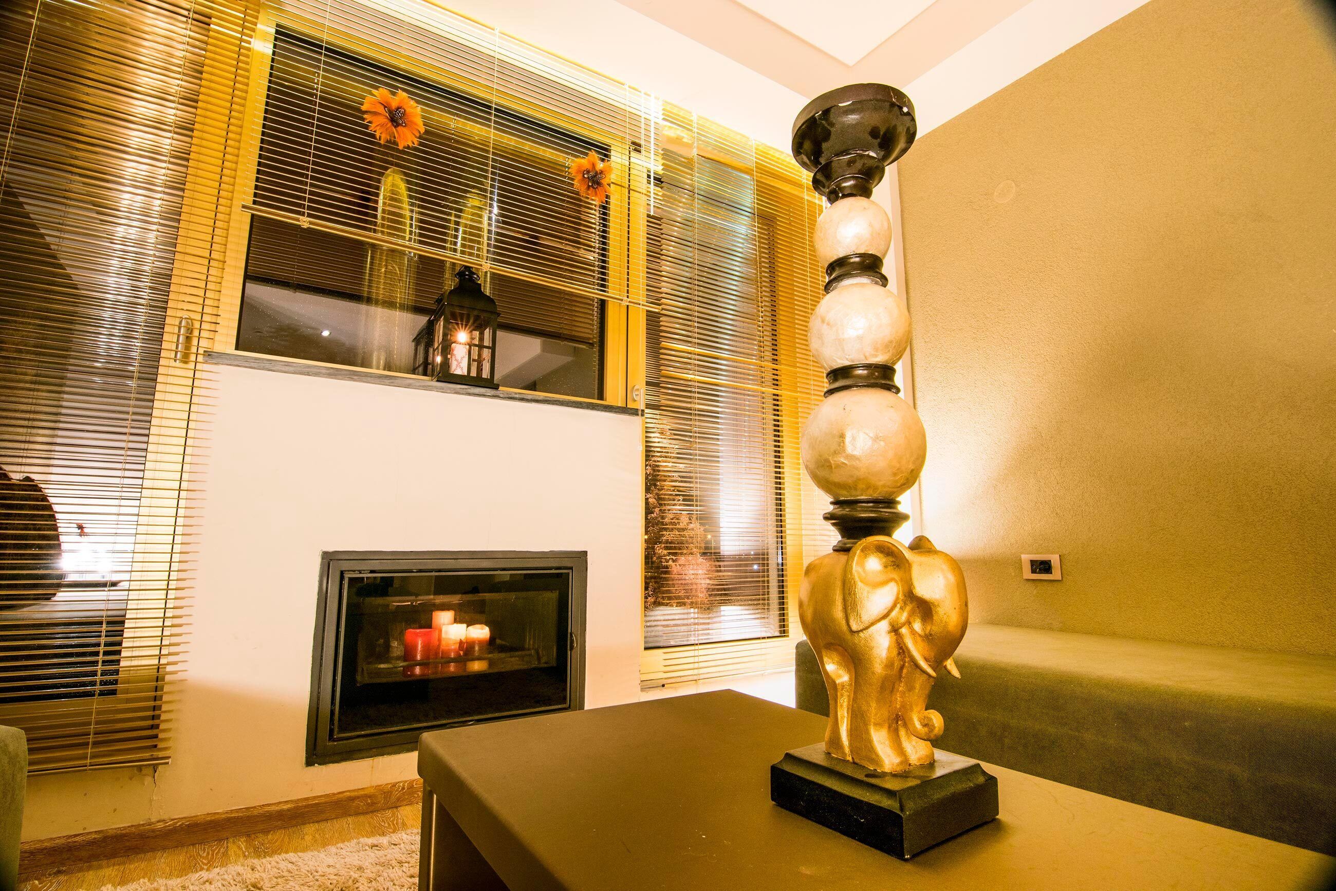 A living room with a fireplace, a decorative elephant sculpture, and a window with blinds.