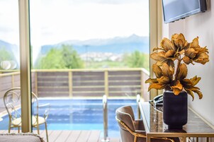 Uma área à beira da piscina com vista para montanhas, uma cadeira, uma mesa com um vaso de flores secas e uma televisão na parede.