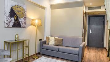 Un salon moderne avec un canapé gris, un tapis à motifs, une lampe sur pied et un élément décoratif mural.