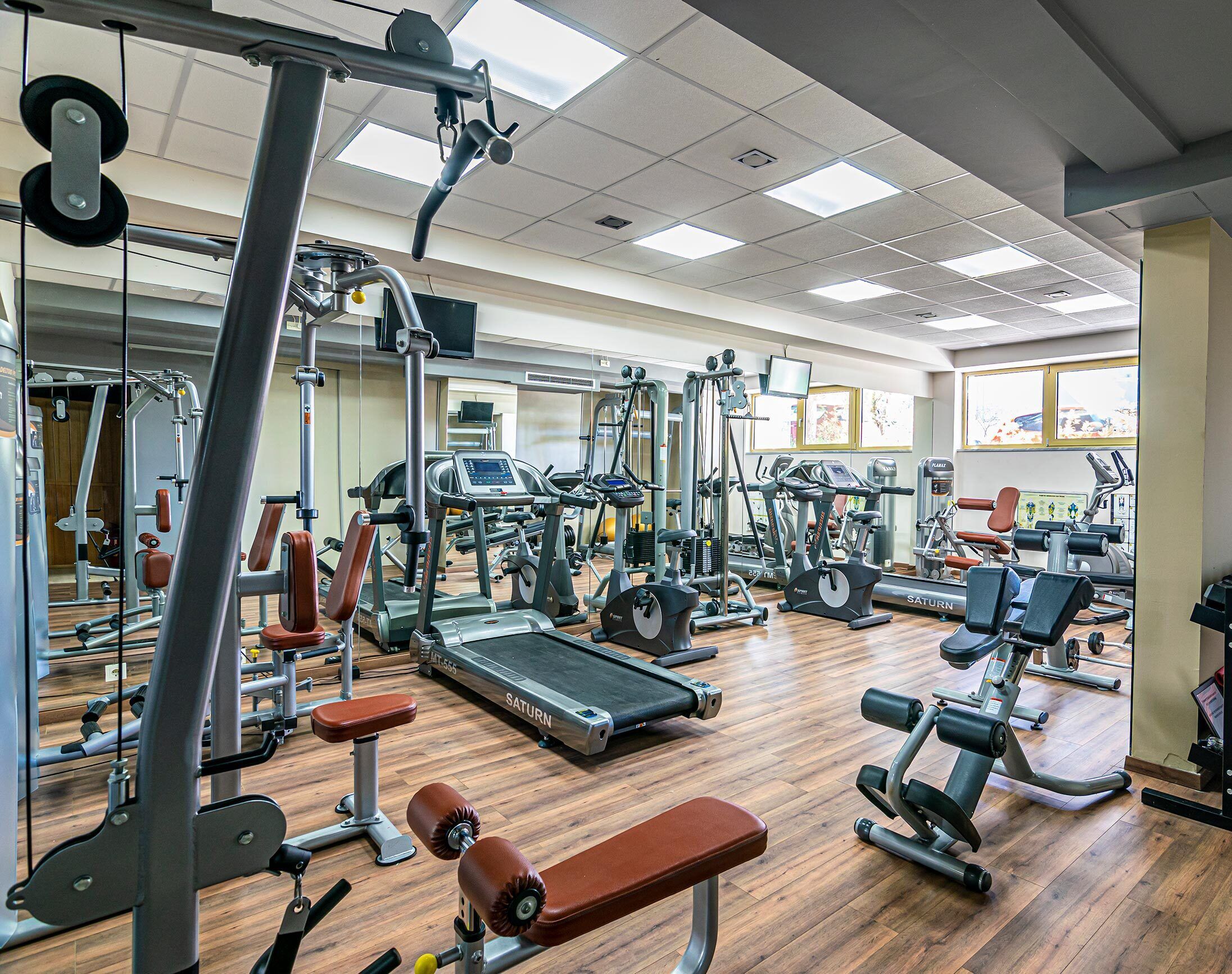 A gym with various exercise machines, a treadmill, and a bench.