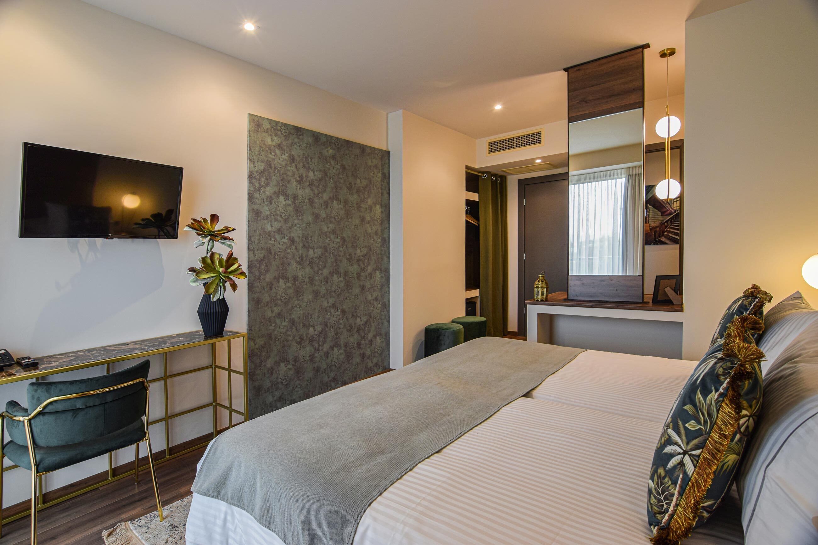 Ein modernes Hotelzimmer mit einem Bett, einem Schreibtisch, einem Sessel, einem Fernseher, einem großen Spiegel und einer Pflanze.