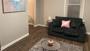 A living room with a dark grey sofa, a small round coffee table, and a painting on the wall.