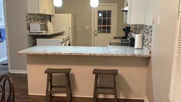 A kitchen with a marble countertop, two stools, wooden flooring, and pendant lighting.