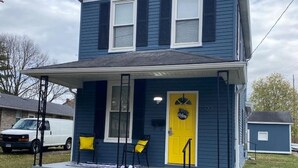 A two-story house with a porch, a yellow door, and a small attached garage.