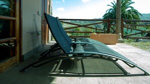 Una tumbona con estructura metálica y cojín, ubicada en un patio con vista a palmeras y un paisaje lejano.