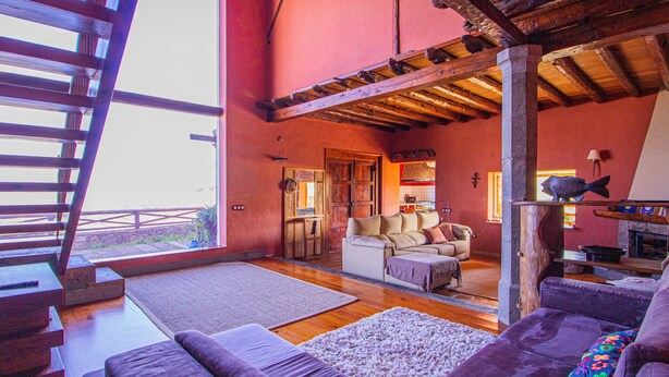 Amplia sala de estar con un ventanal grande, vigas de madera, un sofá y una chimenea.