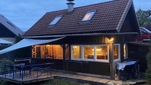 A wooden house with a sloped roof, two skylights, and a covered porch with a blue railing. - Climbing hut Saxon Switzerland ... Wander ... Climb ... Relax (Gossdorf)