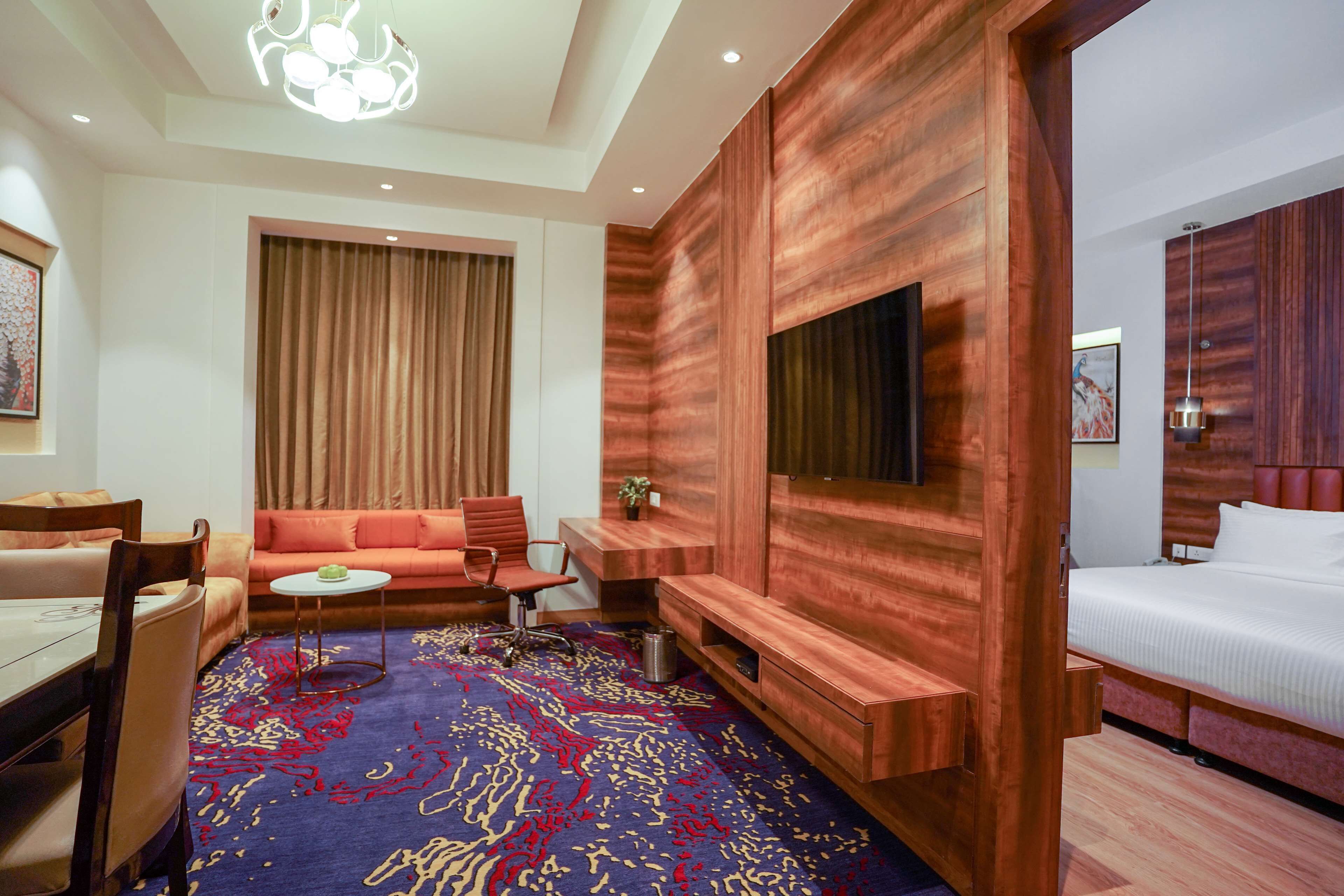 Habitación de hotel con una pared de madera decorativa, una cama grande, un sofá, un televisor, un escritorio y una alfombra estampada.
