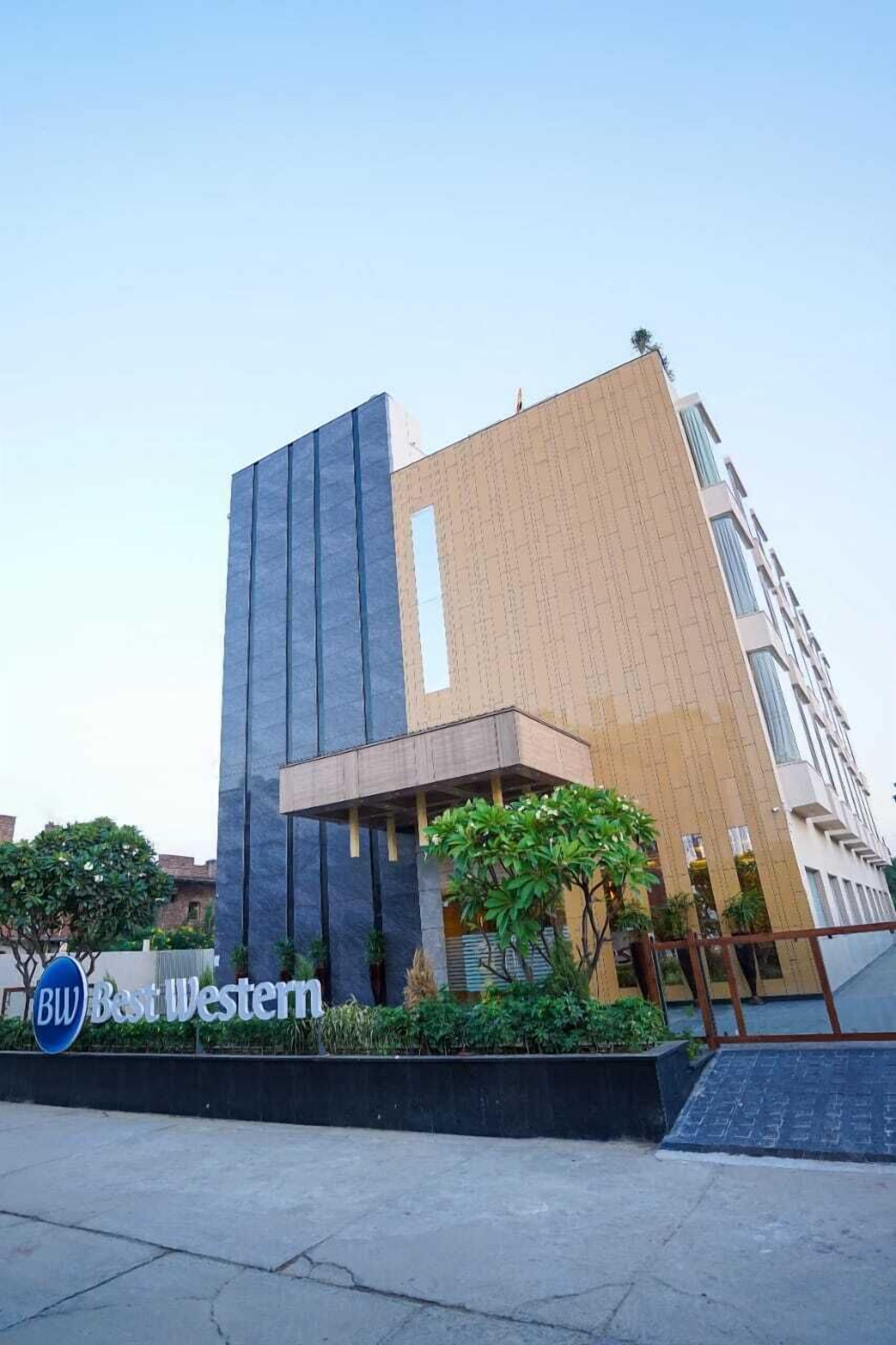 Un edificio moderno con un design verticale marcato, un cartello con su scritto 'BW Best Western' e un'area verde con piante.