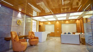 A modern lobby with wooden ceiling, a reception desk, two orange armchairs, and a decorative wall piece.