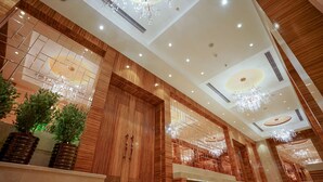A spacious lobby with wooden paneling, large chandeliers, and potted plants.