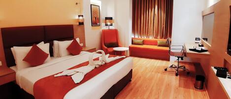 A hotel room with a large bed, a sofa, a desk, and a TV.