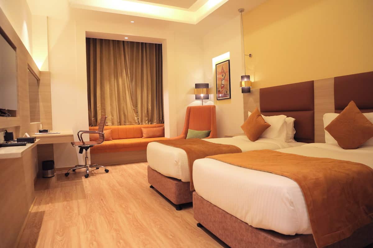 Ein Hotelzimmer mit zwei Betten, einem Schreibtisch, einem Stuhl und einem Fenster mit Vorhängen.