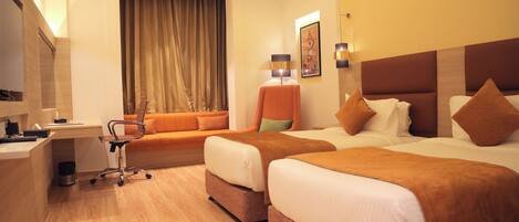 A hotel room with two beds, a desk, a chair, and a window with curtains.