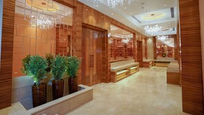 A spacious lobby with wooden paneling, a marble floor, and a large chandelier.