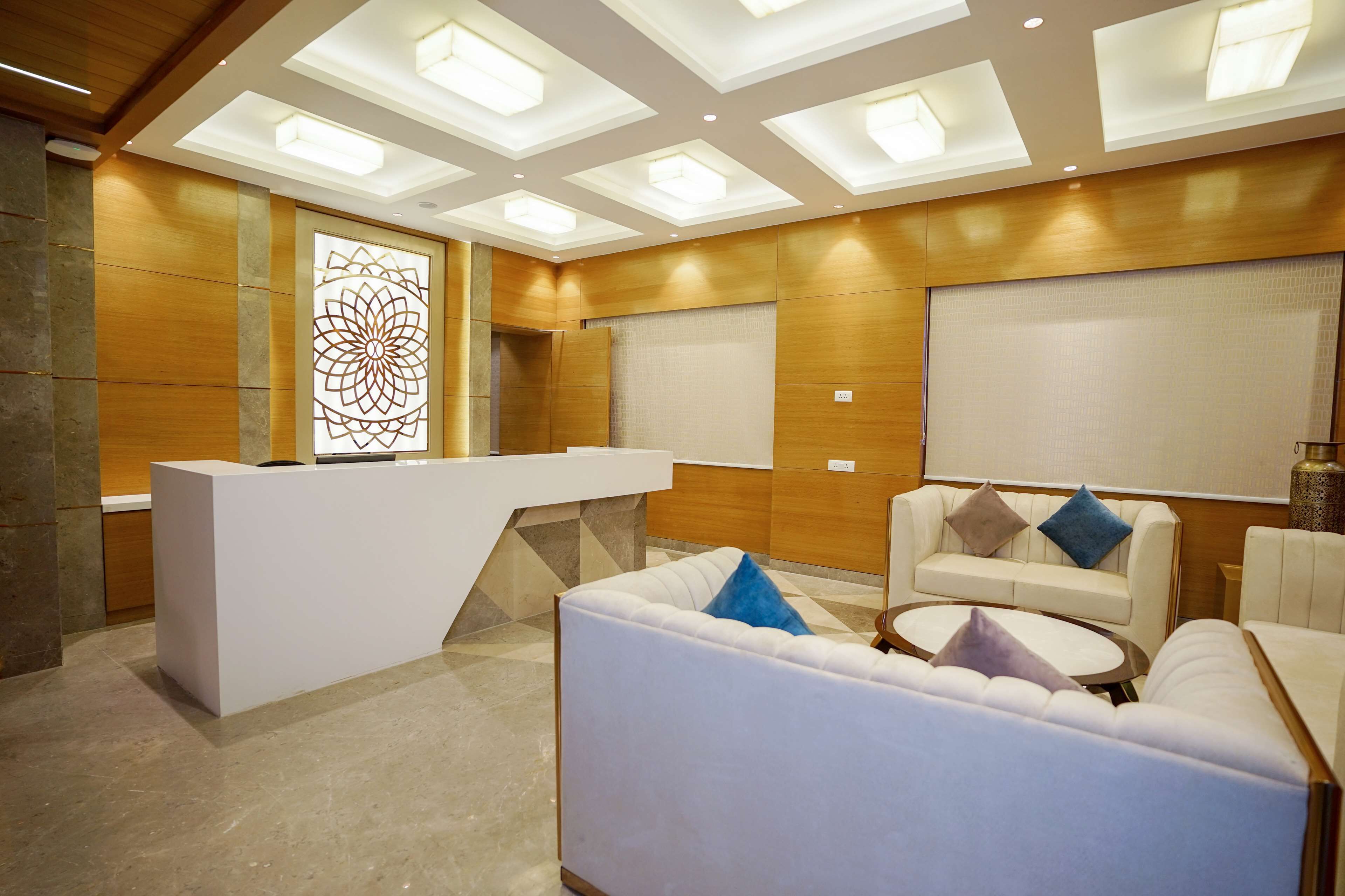 A modern reception area with a white reception desk, a seating area with white sofas and a round table, and a decorative wall panel.