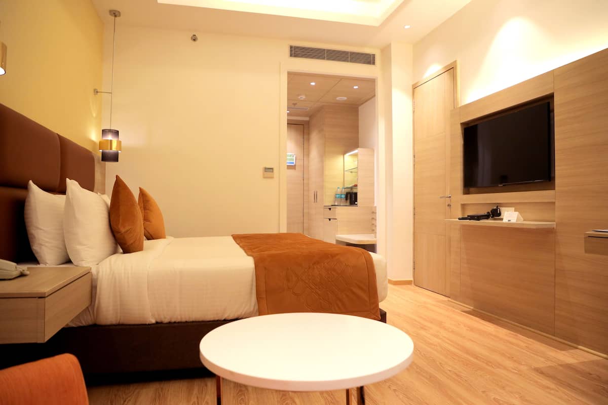 Ein modernes Hotelzimmer mit Bett, Nachttisch, Fernseher und einem kleinen runden Tisch.