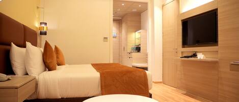 A modern hotel room with a bed, bedside table, TV, and a small round table.
