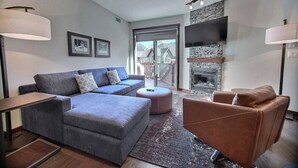 A modern living room with a grey sectional sofa, a brown armchair, and a fireplace.