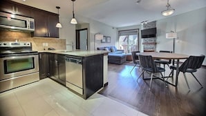 A modern kitchen with stainless steel appliances, a central island, pendant lighting, and a dining area with a table and chairs.