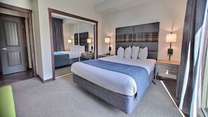 A hotel room with a large bed, a bedside table, a mirror, and a door.