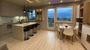 Una cucina moderna con isola centrale, sgabelli da bar, zona pranzo con tavolo e sedie e ampie finestre con vista sulla città.