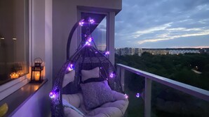 Un balcone con una poltrona amaca decorata con luci viola, un lanternino e vista sulla città.