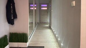 Un corridoio moderno con una porta in vetro, una giacca nera appesa al muro e una piccola pianta verde.