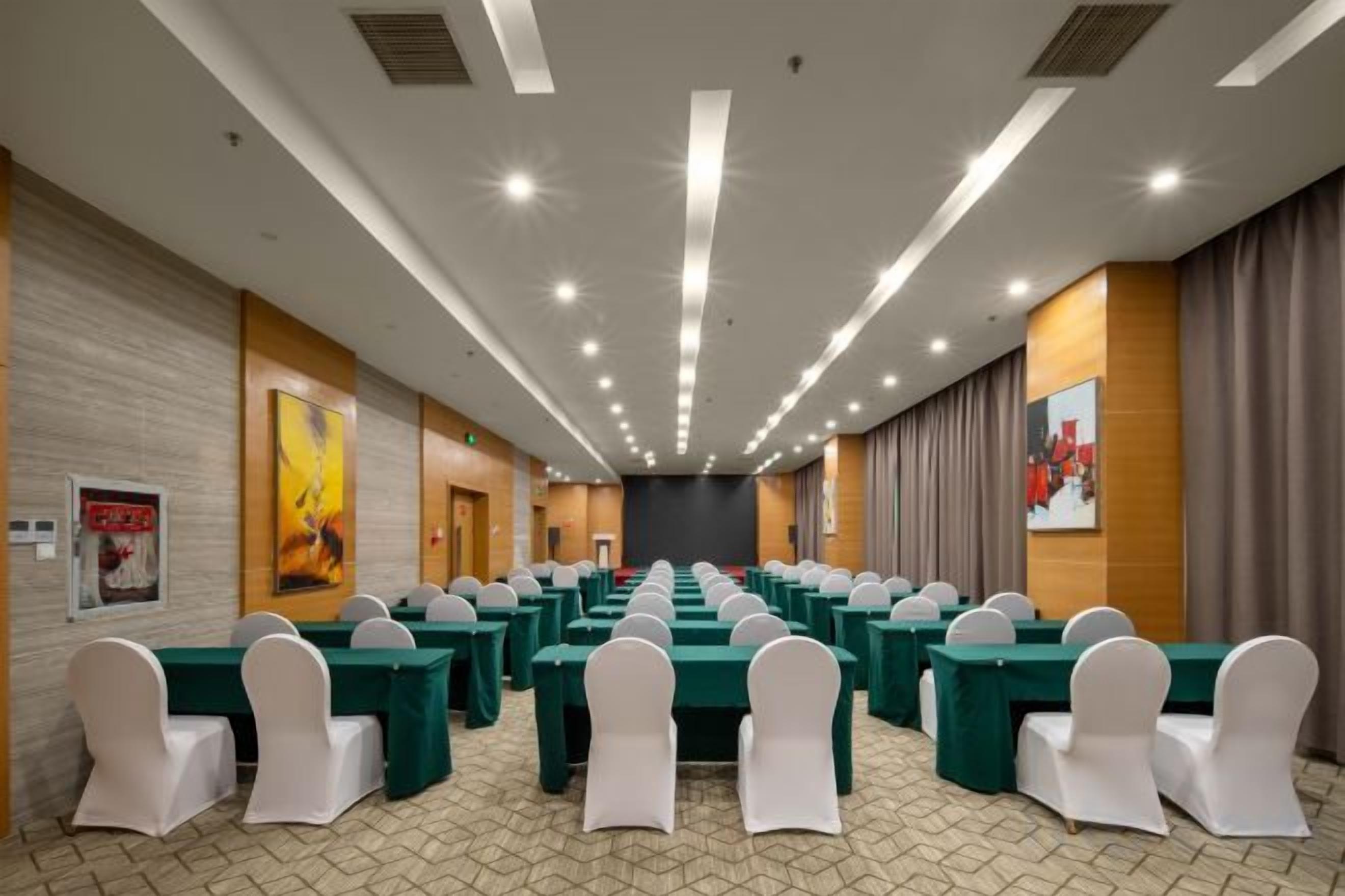 A conference room with rows of tables and chairs, a wooden wall, and a large painting.