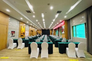A conference room with rows of tables and chairs, a stage at the front, and a large window on the right. - Tenglong Hotel (Kaili)