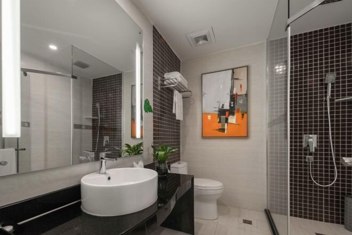 A modern bathroom with a large mirror, a round sink, a toilet, and a shower area.