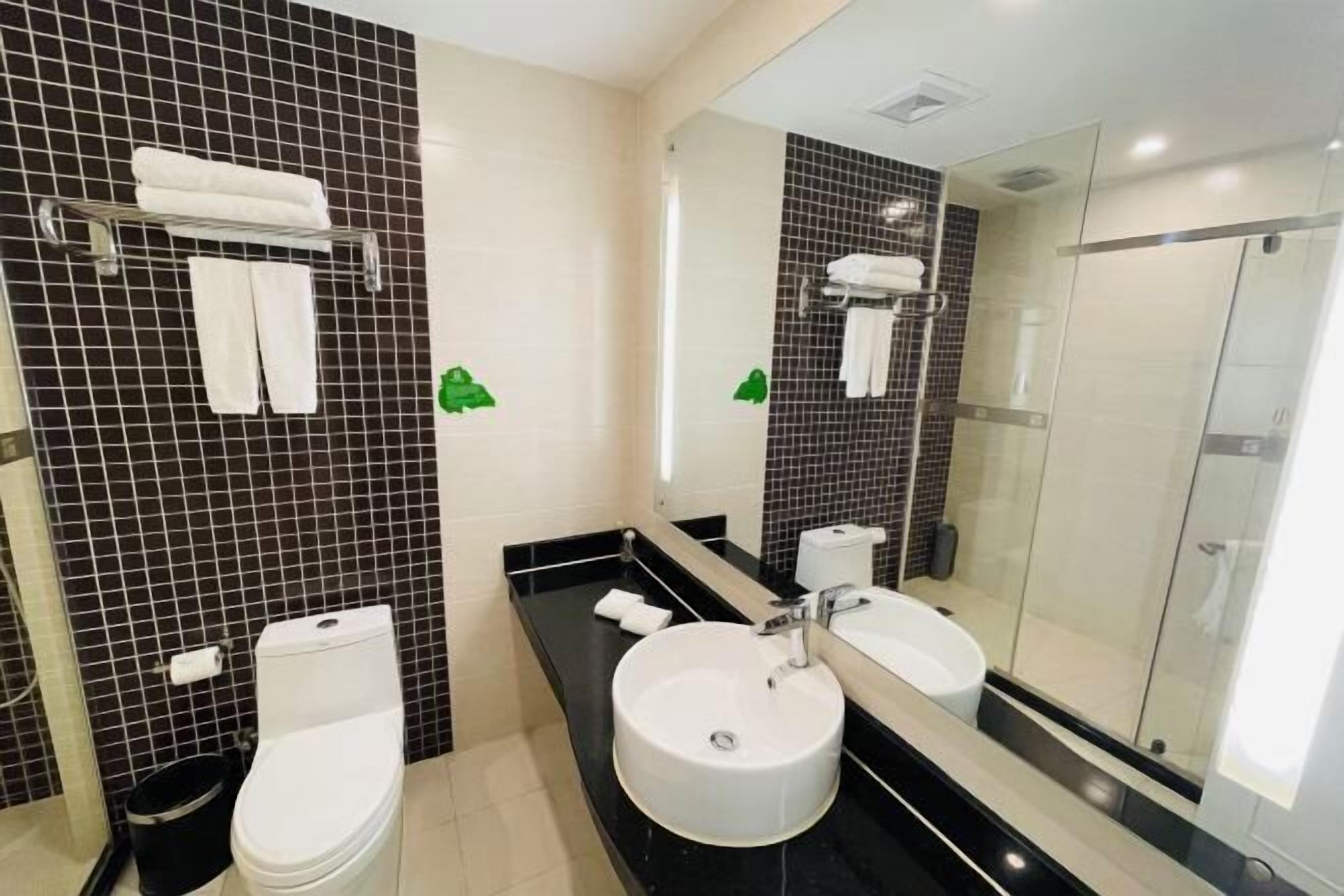 A modern bathroom with a black and white tiled wall, a white toilet, a round sink, and a glass shower enclosure.