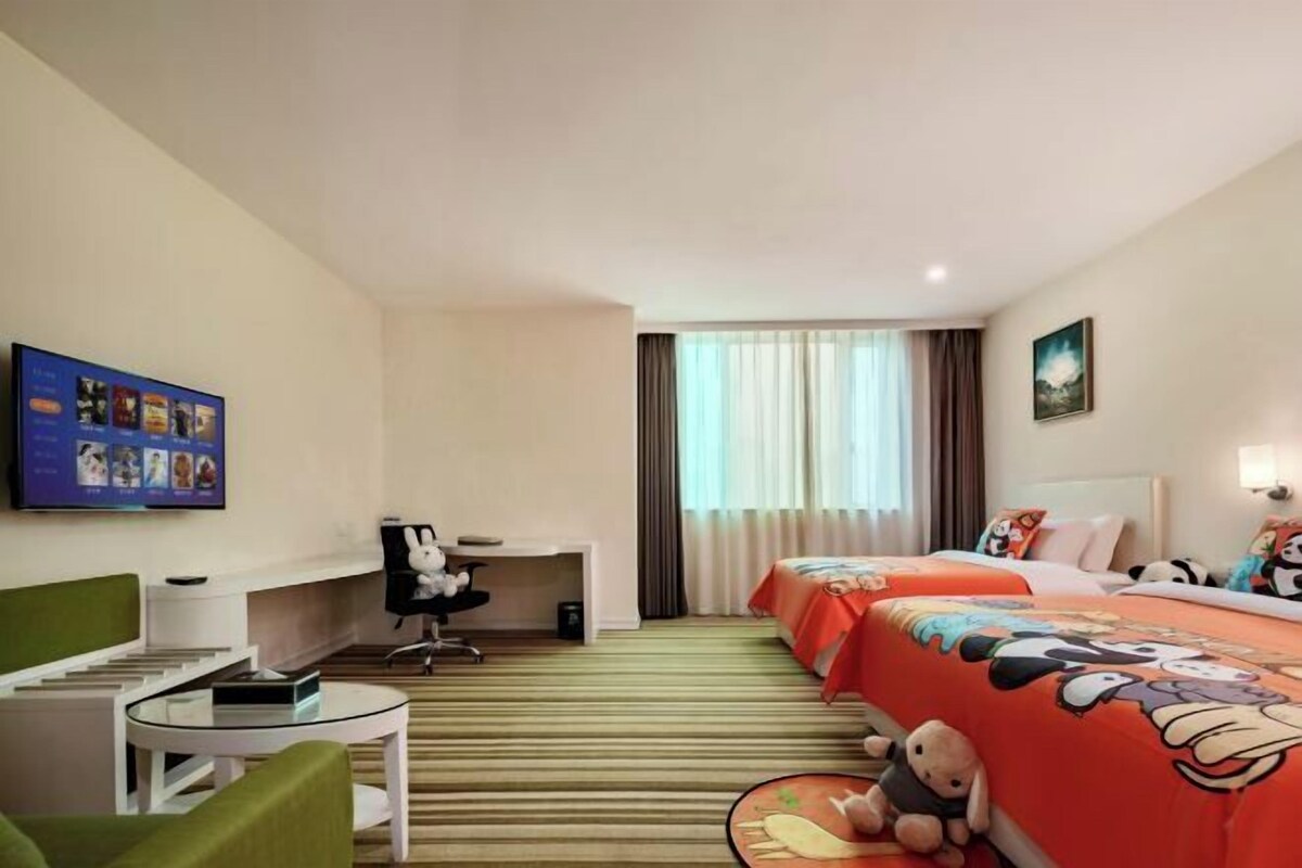 A hotel room with two beds, a desk, a chair, and a television on the wall.