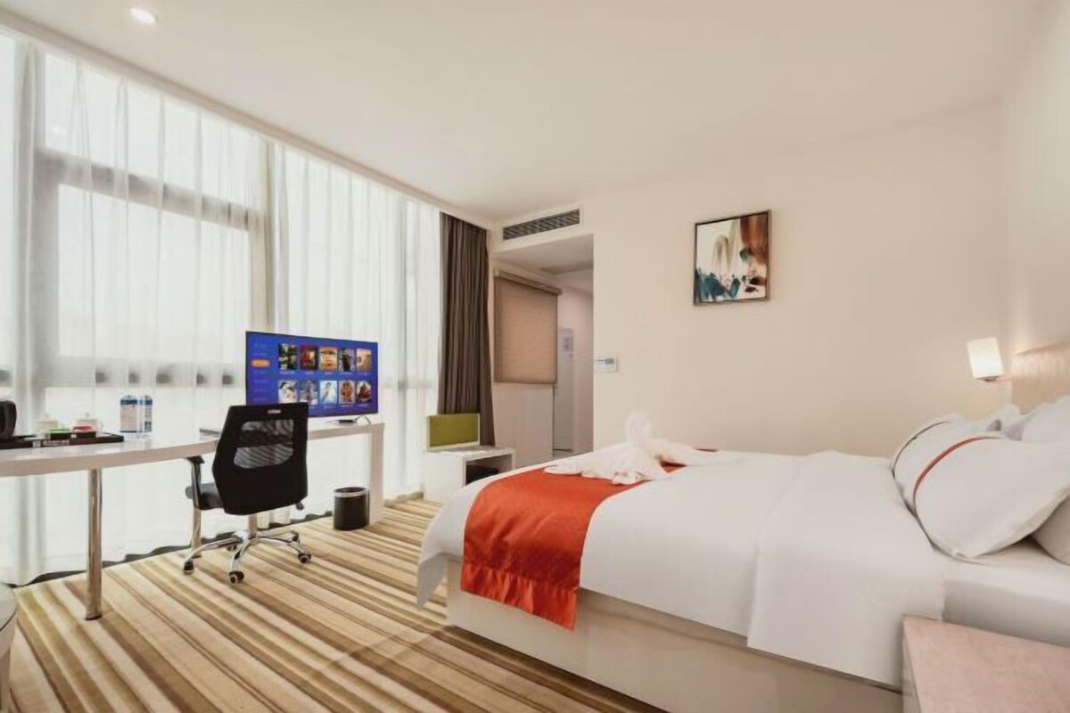 A hotel room with a bed, a desk, a chair, and a large window.