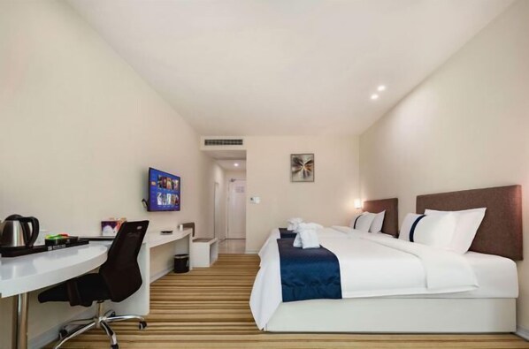 Habitación de hotel con cama, escritorio y silla. Hay un televisor en la pared y un cuadro sobre la cama.