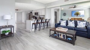A modern living room with a sofa, coffee table, and chairs. There is a kitchen area with a bar and seating.