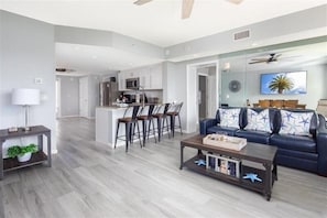Un salon moderne avec un canapé, une table basse et des fauteuils. Il y a également un coin cuisine avec un bar et des sièges.