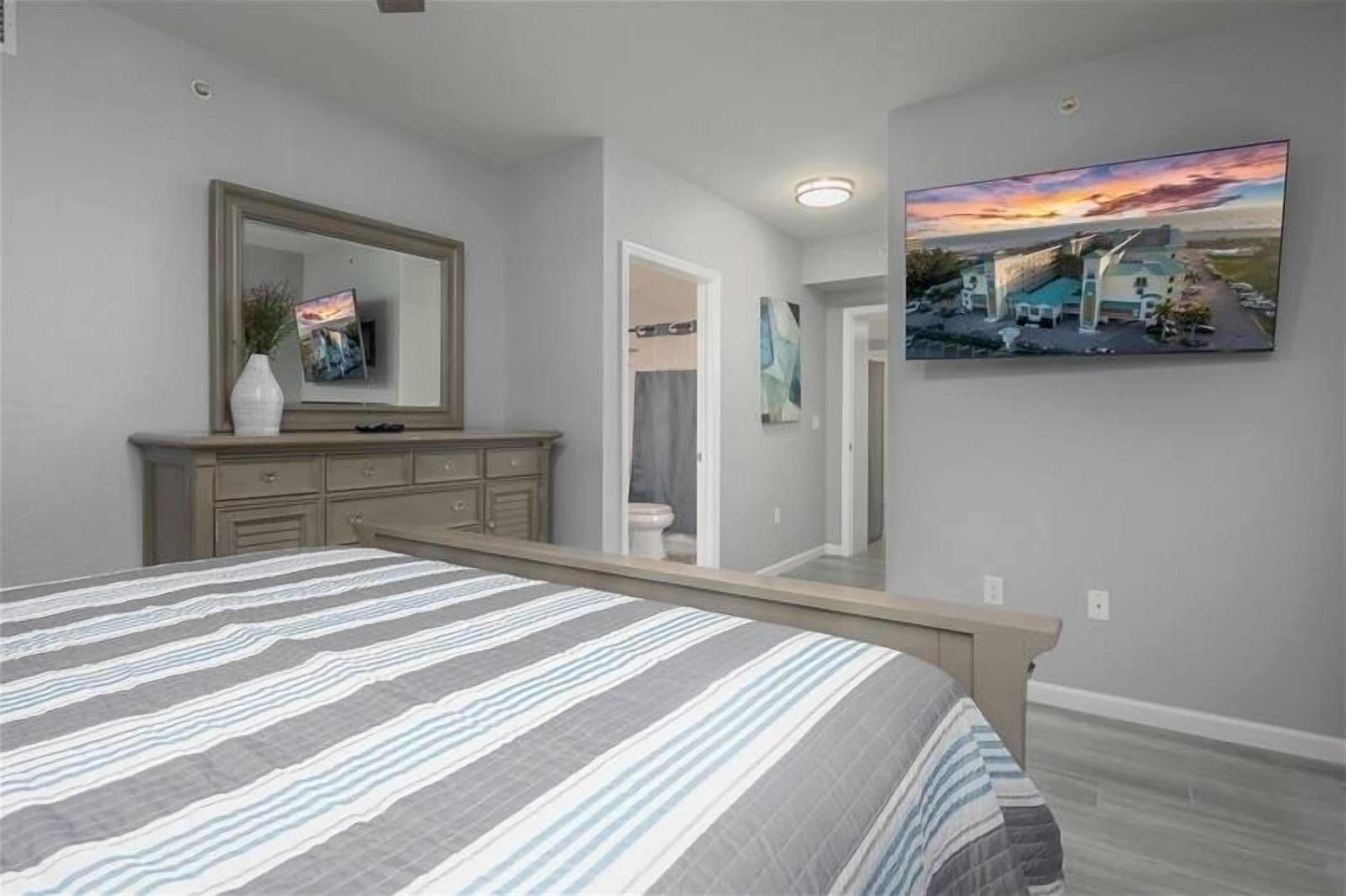 A bedroom with a bed, dresser, mirror, and artwork on the wall.