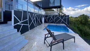 Un espace piscine extérieur moderne, agrémenté d’un mur au design géométrique, d’une chaise longue et d’un escalier menant à un deuxième niveau.