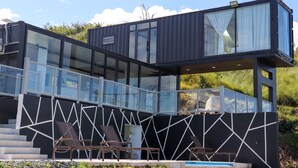 Un bâtiment moderne à deux étages, doté de grandes fenêtres en verre, d’une piscine et d’un espace extérieur aménagé pour s’asseoir.