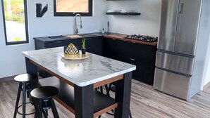 Une cuisine moderne dotée d’un îlot en marbre, de tabourets de bar noirs, d’un réfrigérateur en acier inoxydable et de meubles de cuisine noirs.