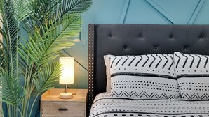 Een bed met gekleurde kussens, een bedlamp en een nachtkastje van hout.