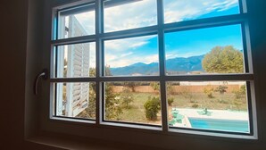 Una ventana con vistas a un patio trasero, que incluye una piscina y montañas al fondo.