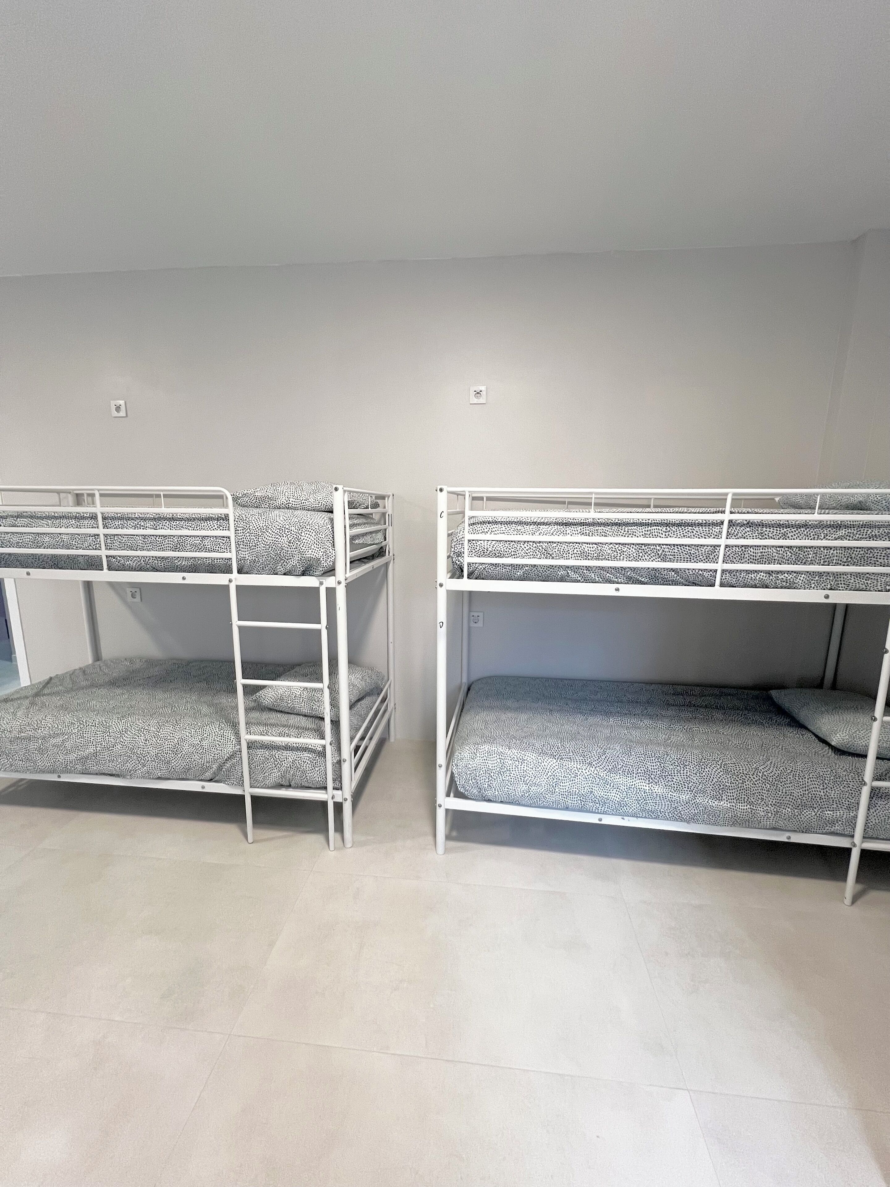 Duas beliches com roupa de cama estampada num quarto com paredes lisas e chão de azulejos.