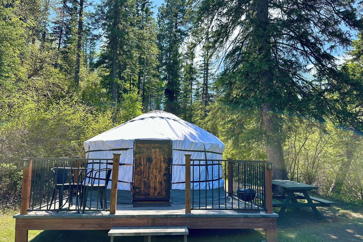A yurt with a wooden deck and a picnic table in a forest setting.