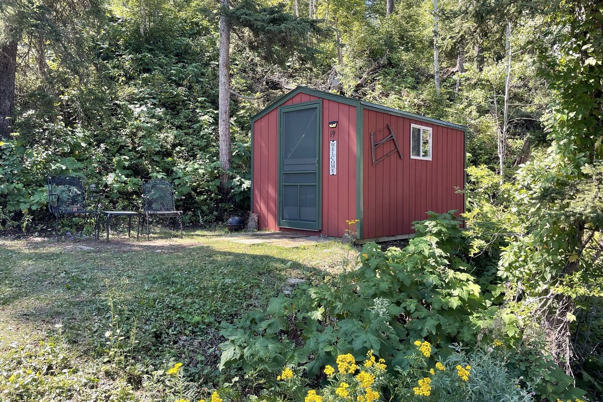 A red shed with a green door, surrounded by dense greenery and trees.