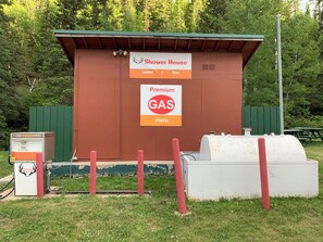 A small, single-story building with a brown exterior and a green roof, labeled as a "Shower House" for both ladies and men, and a sign indicating "Premium GAS Here." - Whitetail Creek Camping Resort (Lead)