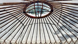 A cozy, circular yurt-style room with a bed, pillows, and a small table with a lantern. - Whitetail Creek Camping Resort (Lead)